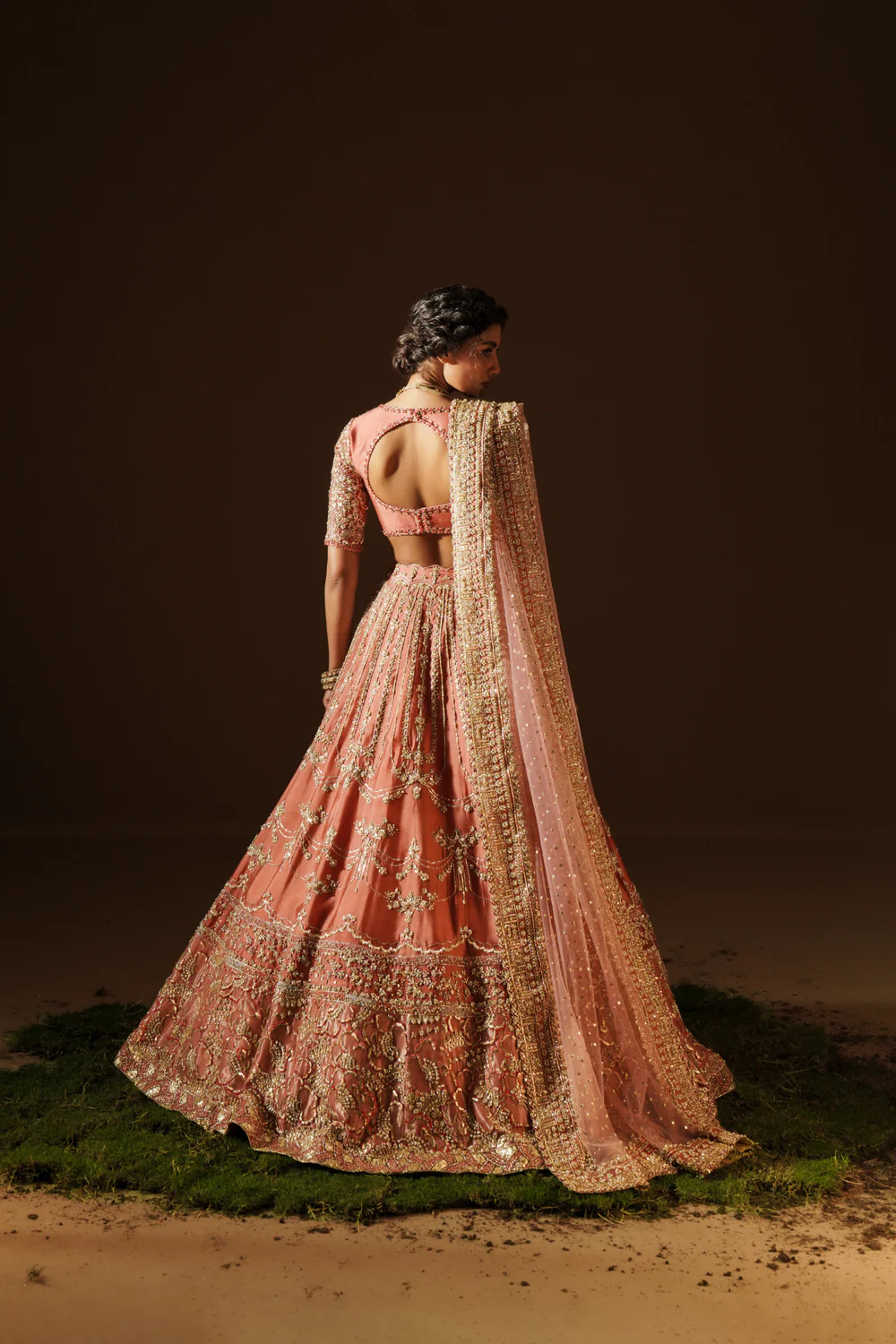 Model_in_a_back_view_angle_wearing_a_warm_coral_handcrafted_raw_silk_lehenga_choli_paired_with_a_net_dupatta